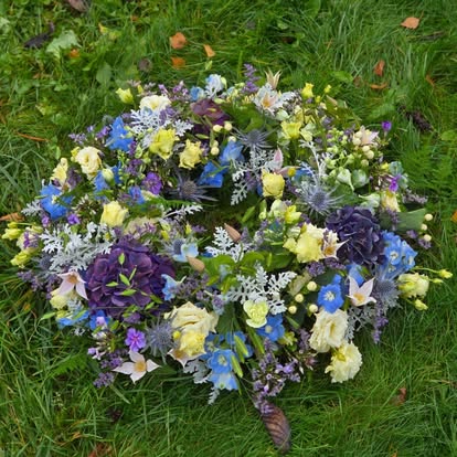 Blomsterkrans i blå, lilla, hvide og lysegule nuancer lagt på græs