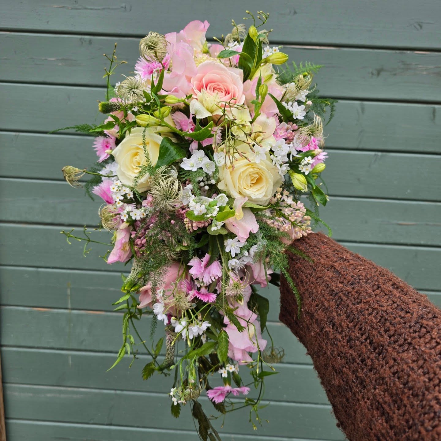 Lang buket med rosa og cremefarvede roser, små hvide blomster og grønt