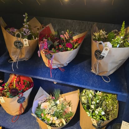 Farverige buketter pakket i papir og stillet på blå hylder i blomsterboden